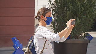 Frau mit Smartphone und Mundschutz mit Europafahne